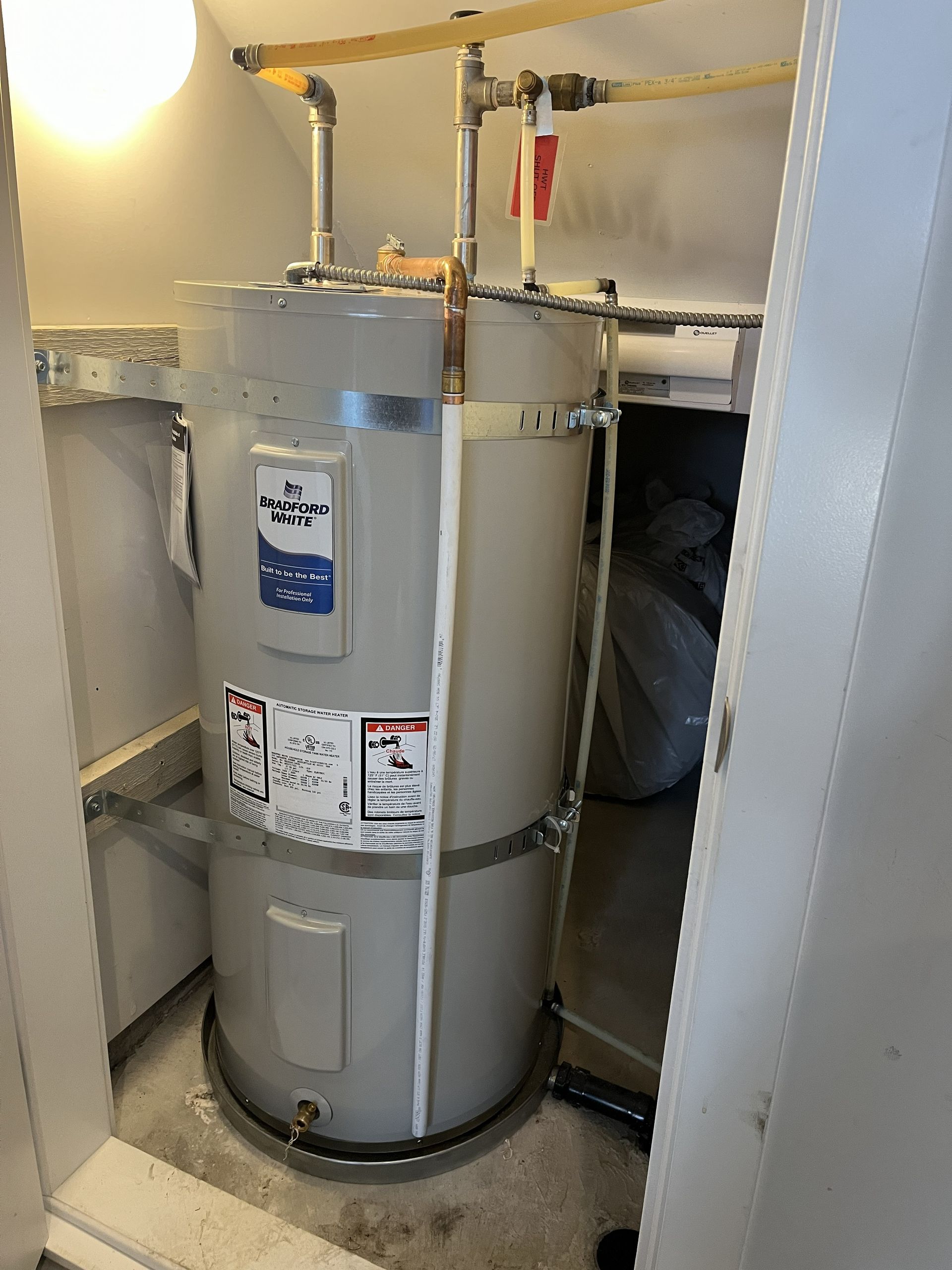Large gray water heater/tank in a utility closet with pipes and valves on top.