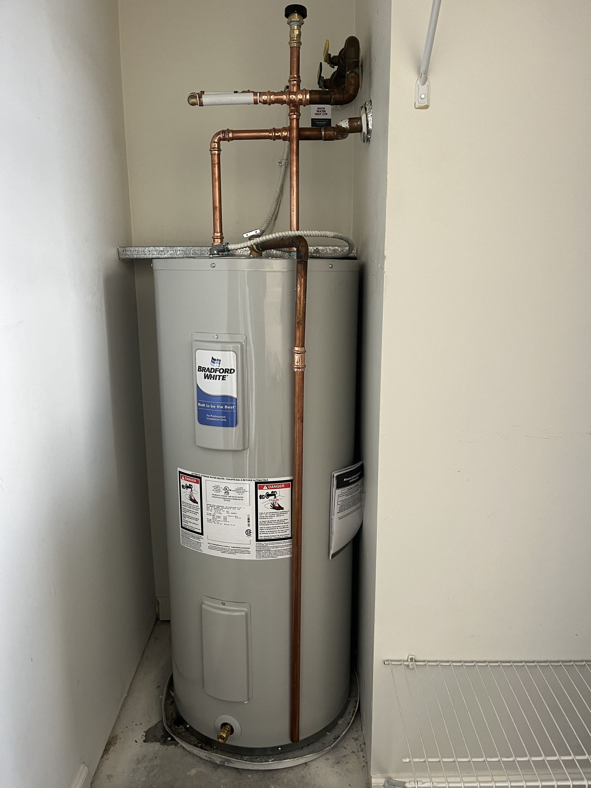 Water heater in a narrow utility closet, with copper pipes and a vented top.