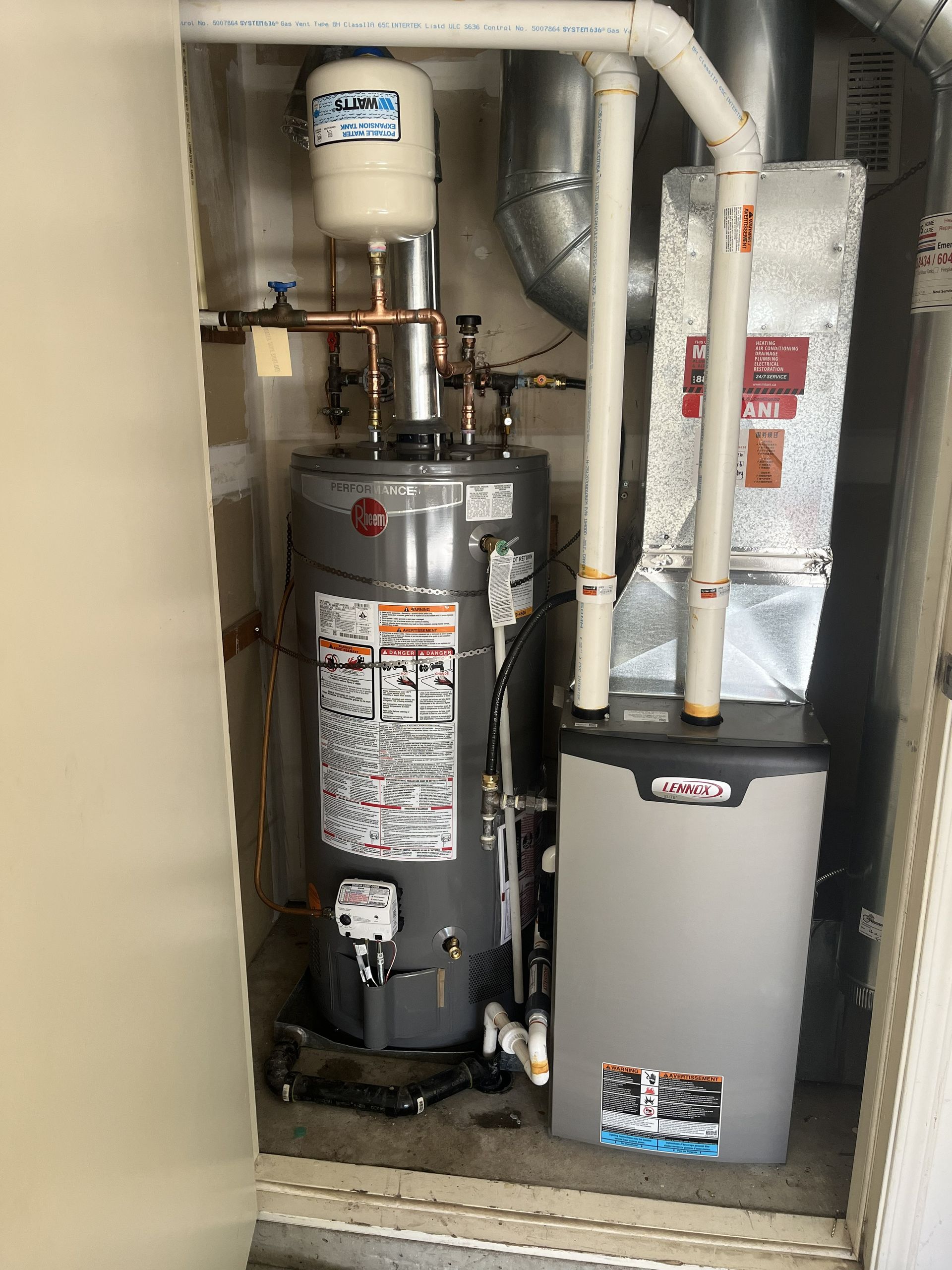Water heater, furnace, and HVAC equipment in a cramped utility closet with white pipes and ductwork.