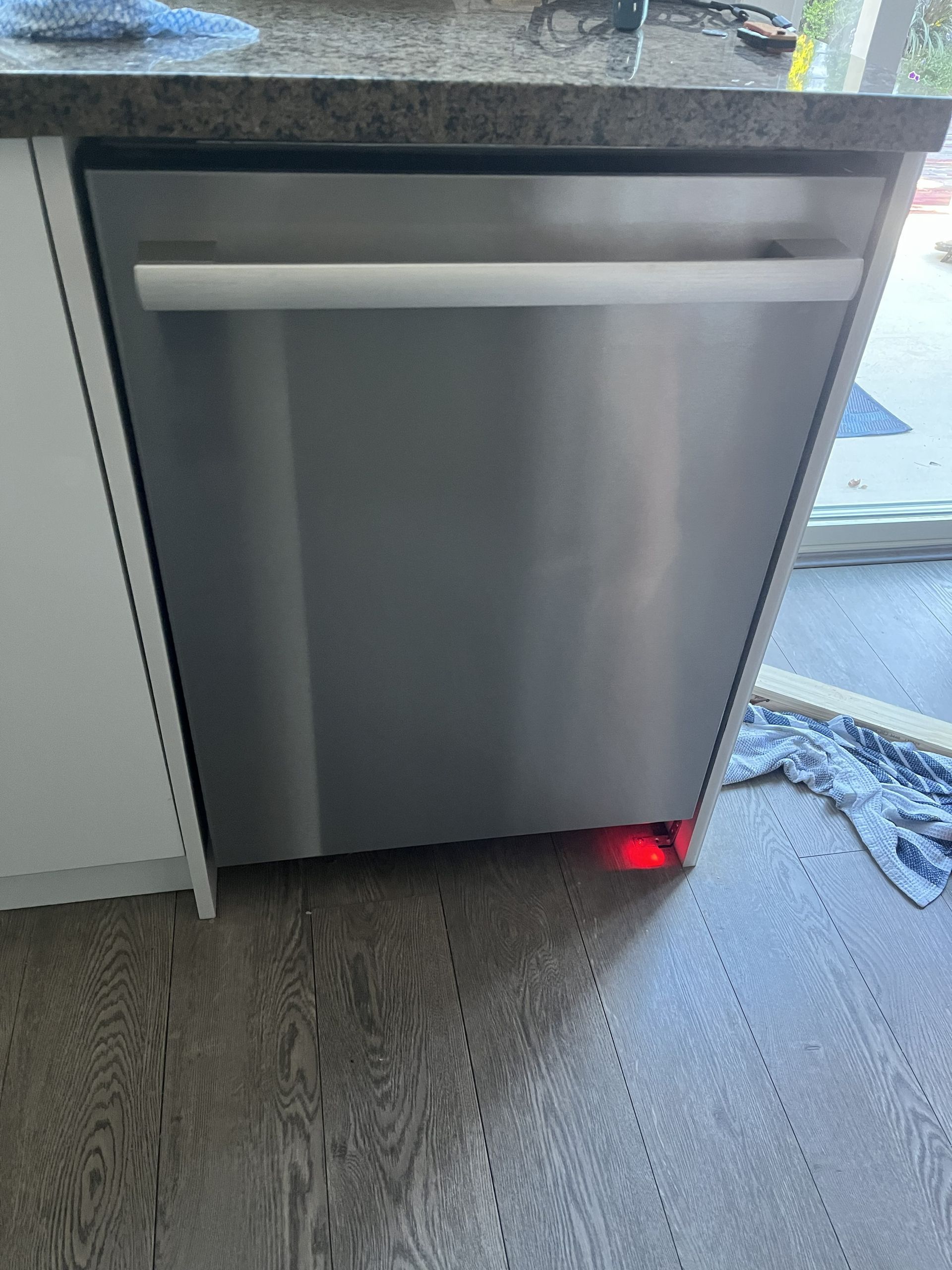 Stainless steel dishwasher under a kitchen counter with a red light glowing at the bottom right.