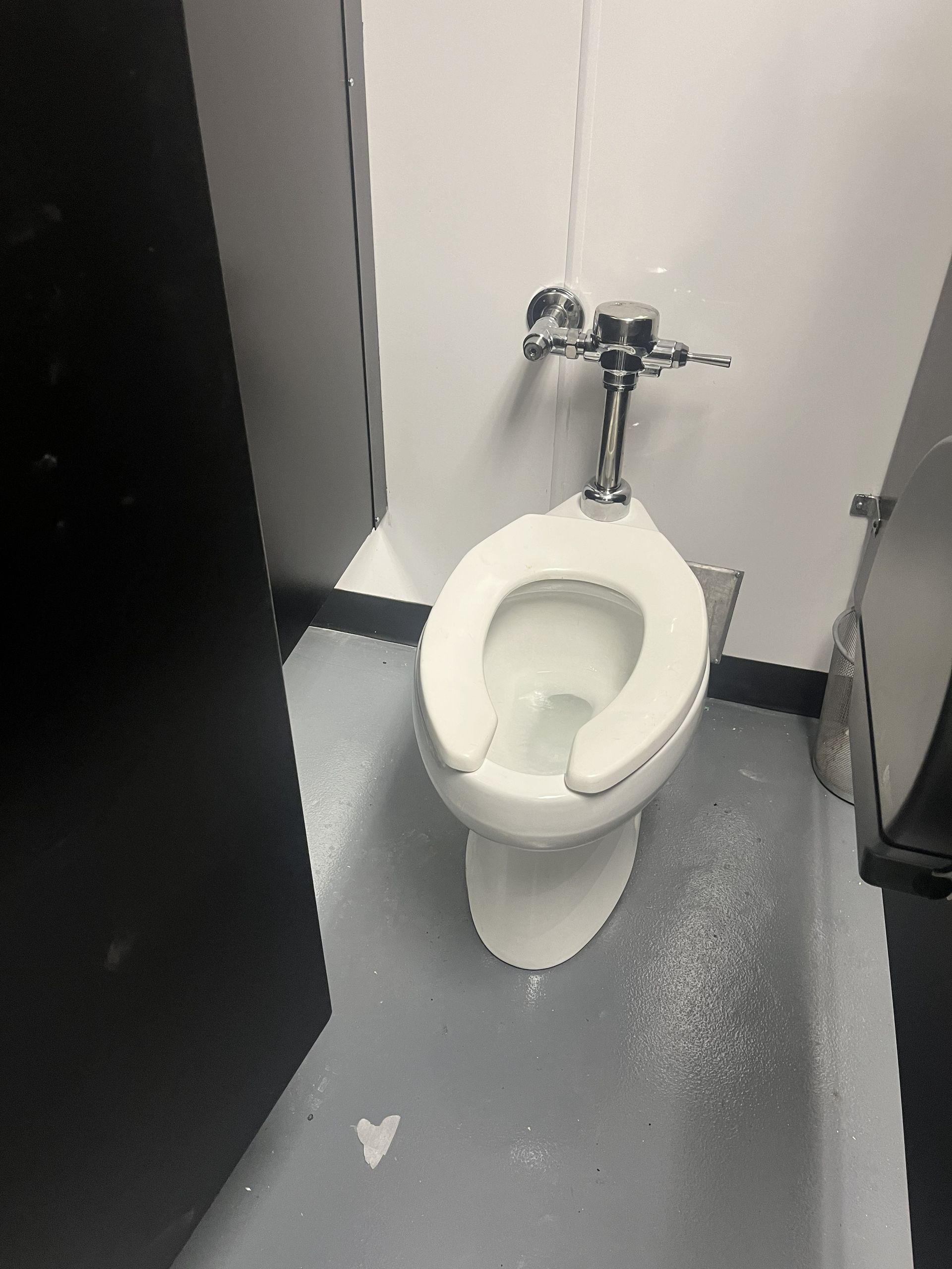 Single white toilet in a small restroom with gray floor and white walls.