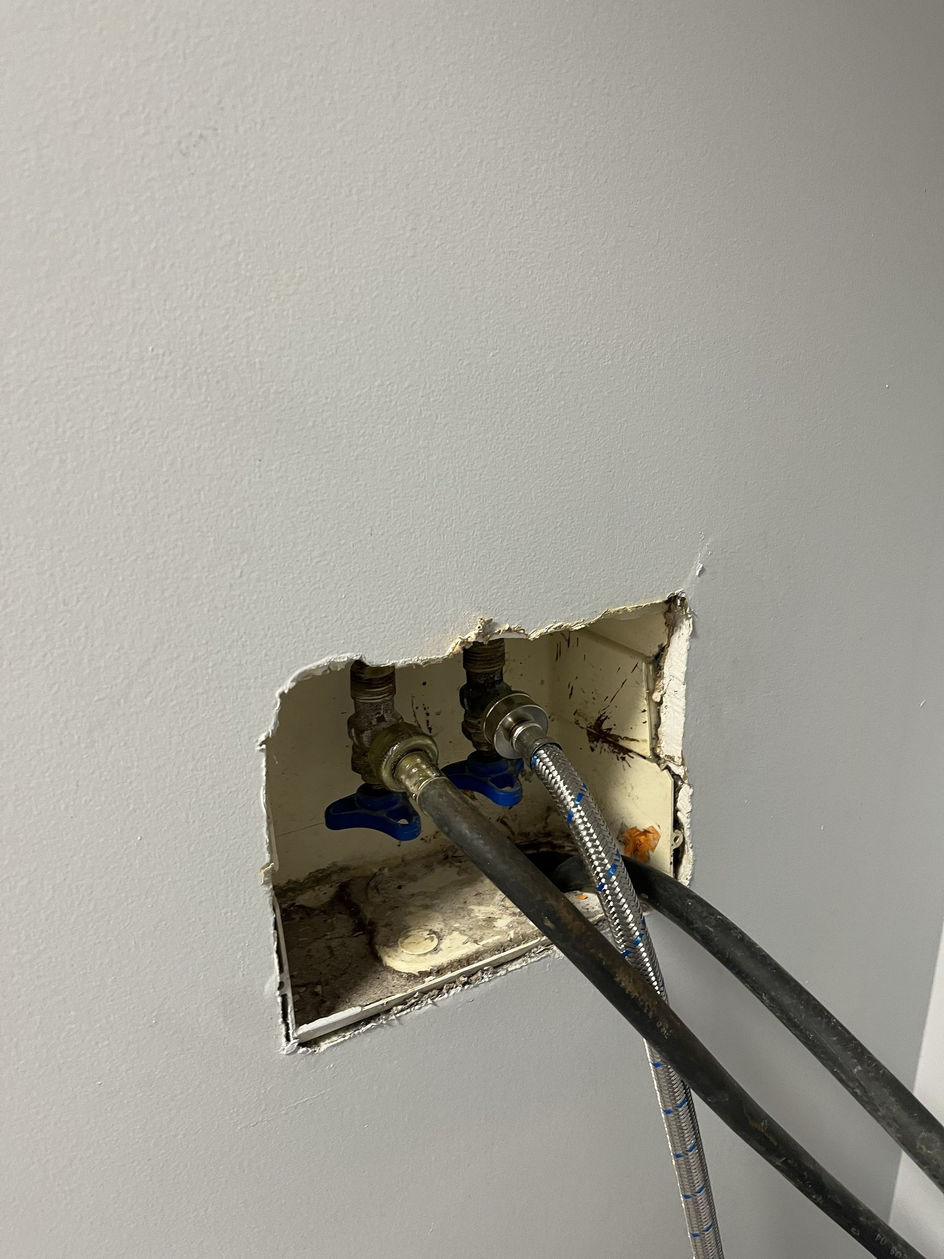 Damaged wall outlet with exposed wires and a cut opening in drywall