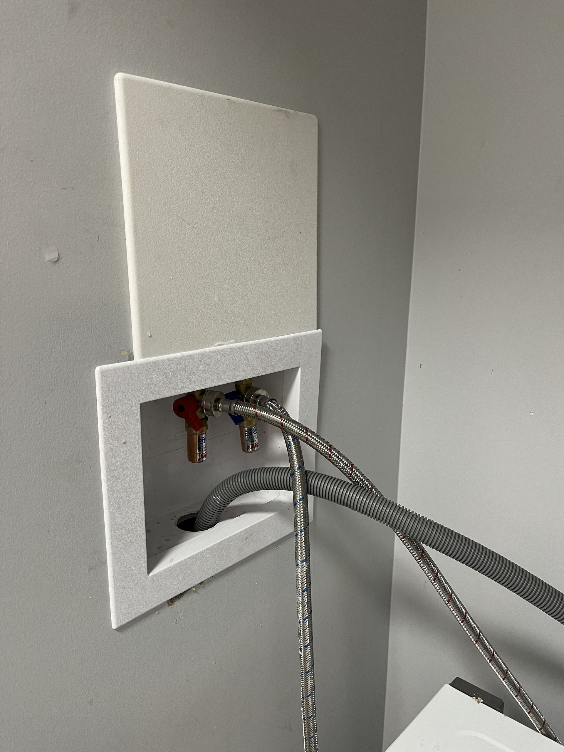 Open wall box with exposed braided cables emerging from a square cutout on a gray wall