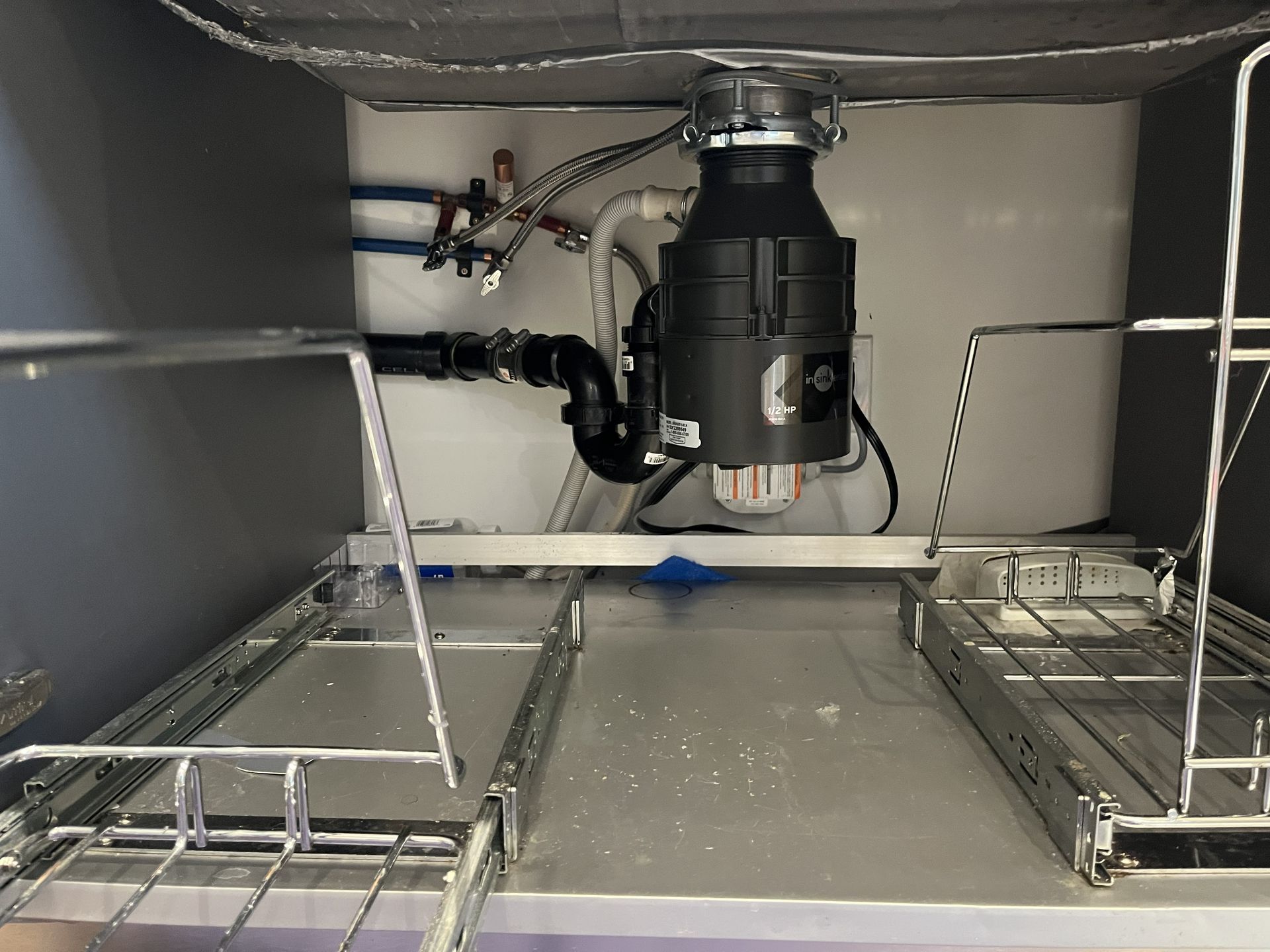 Under-sink cabinet with a garbage disposal, pipes, and wire dish racks on both sides