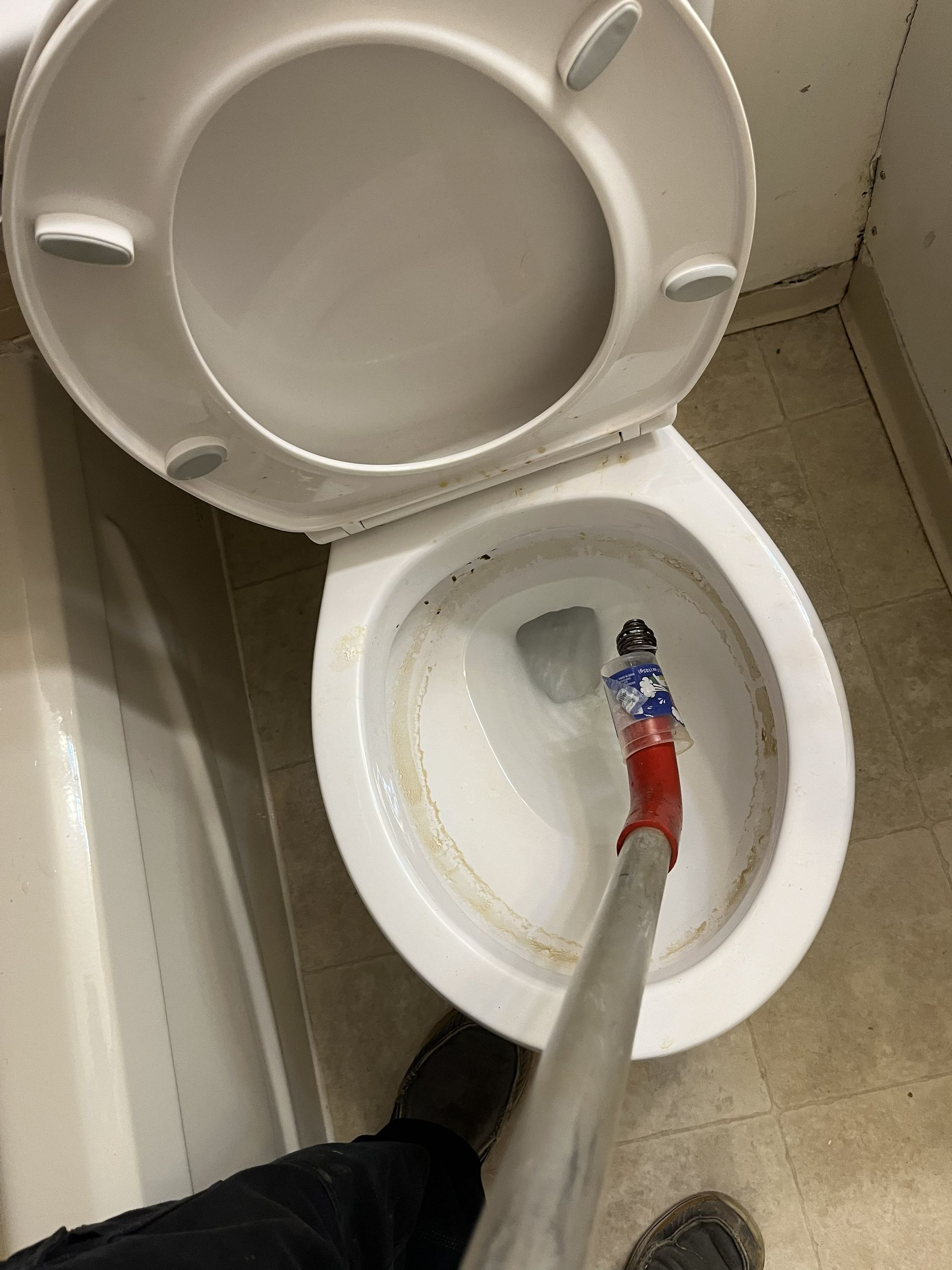 Toilet with the seat up and a hose being used inside the bowl.