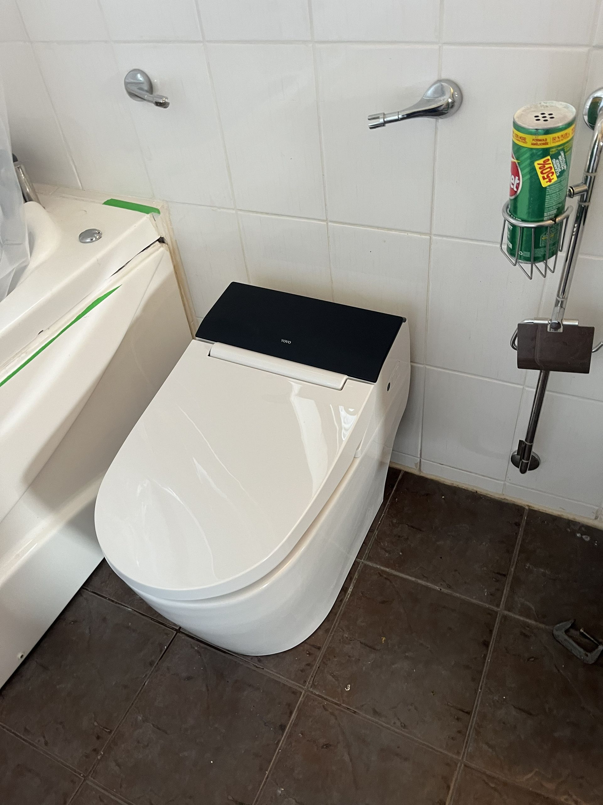 Bathroom with a white toilet and black seat cover on dark tile floor, beside a wall-mounted toilet brush holder.