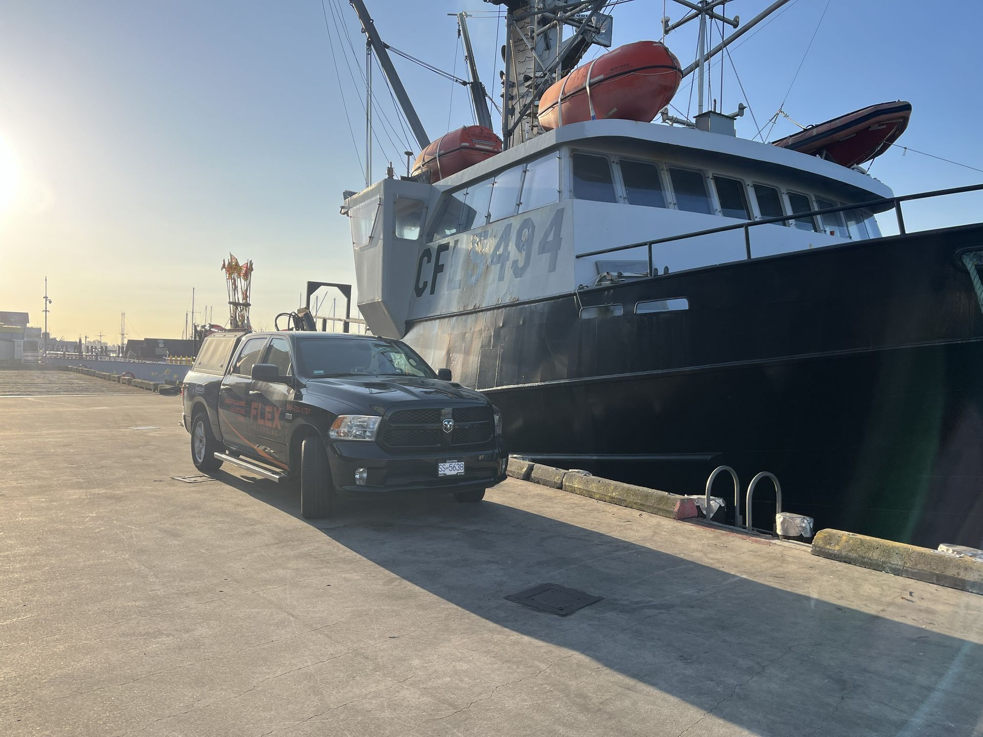 Black car parked beside a large fishing boat at a harbor in warm evening light