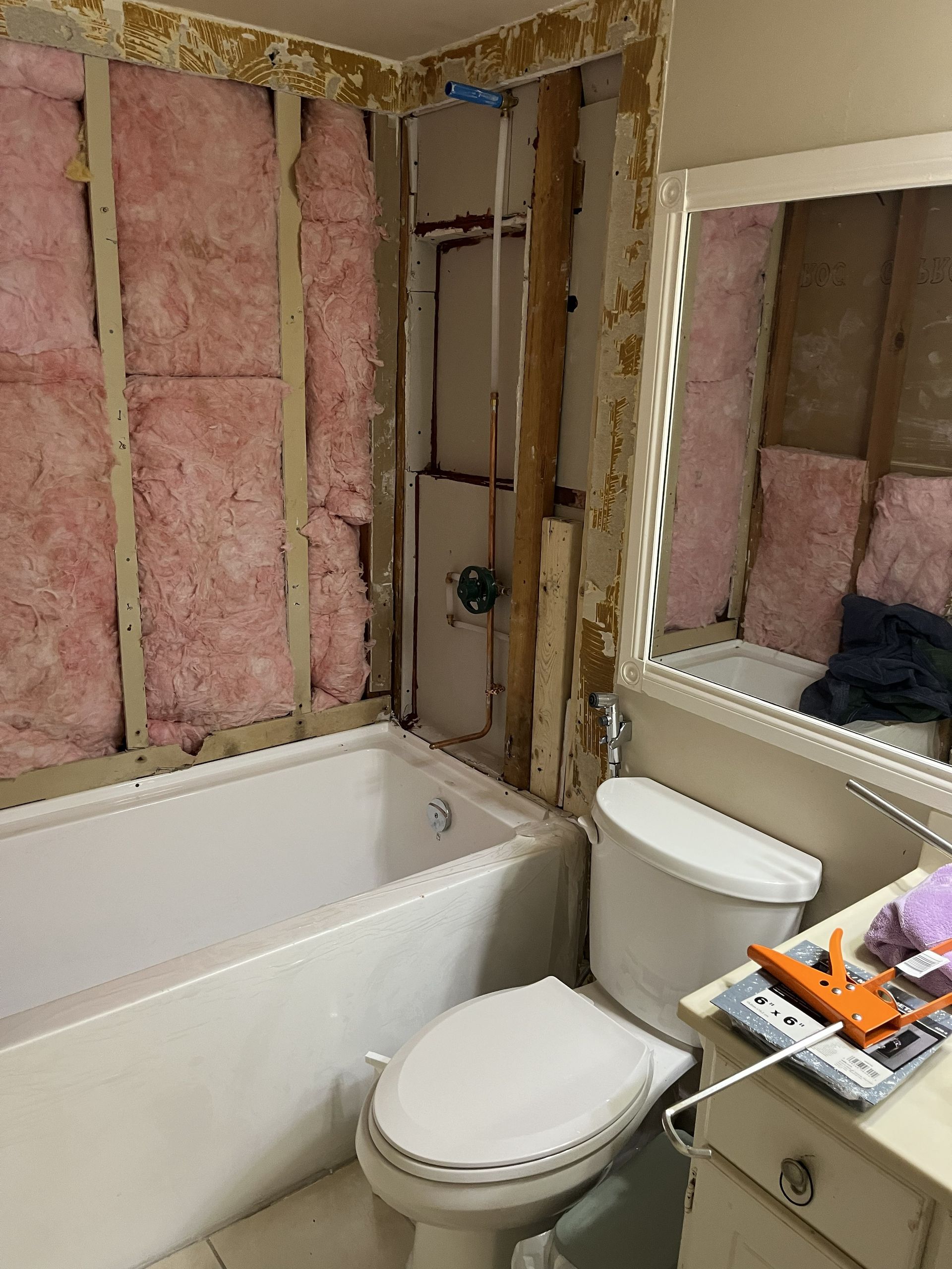 Partially renovated bathroom with pink insulation, bathtub, toilet, and mirror cabinet