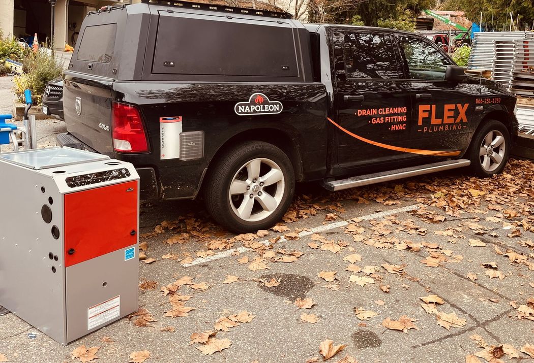 Black utility van with orange “FLEX” lettering parked on a leaf-covered street beside a red machine.
