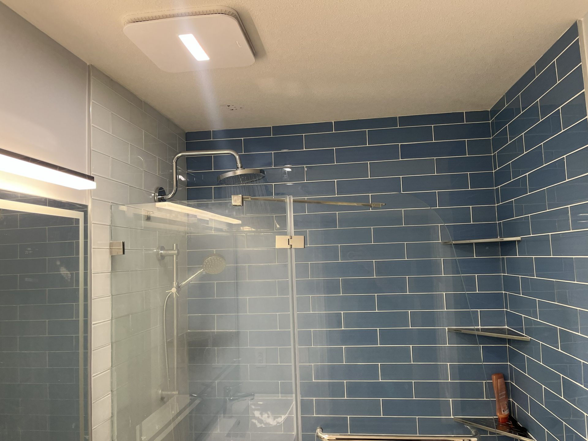Blue-tiled bathroom with glass shower enclosure and mirror sink area