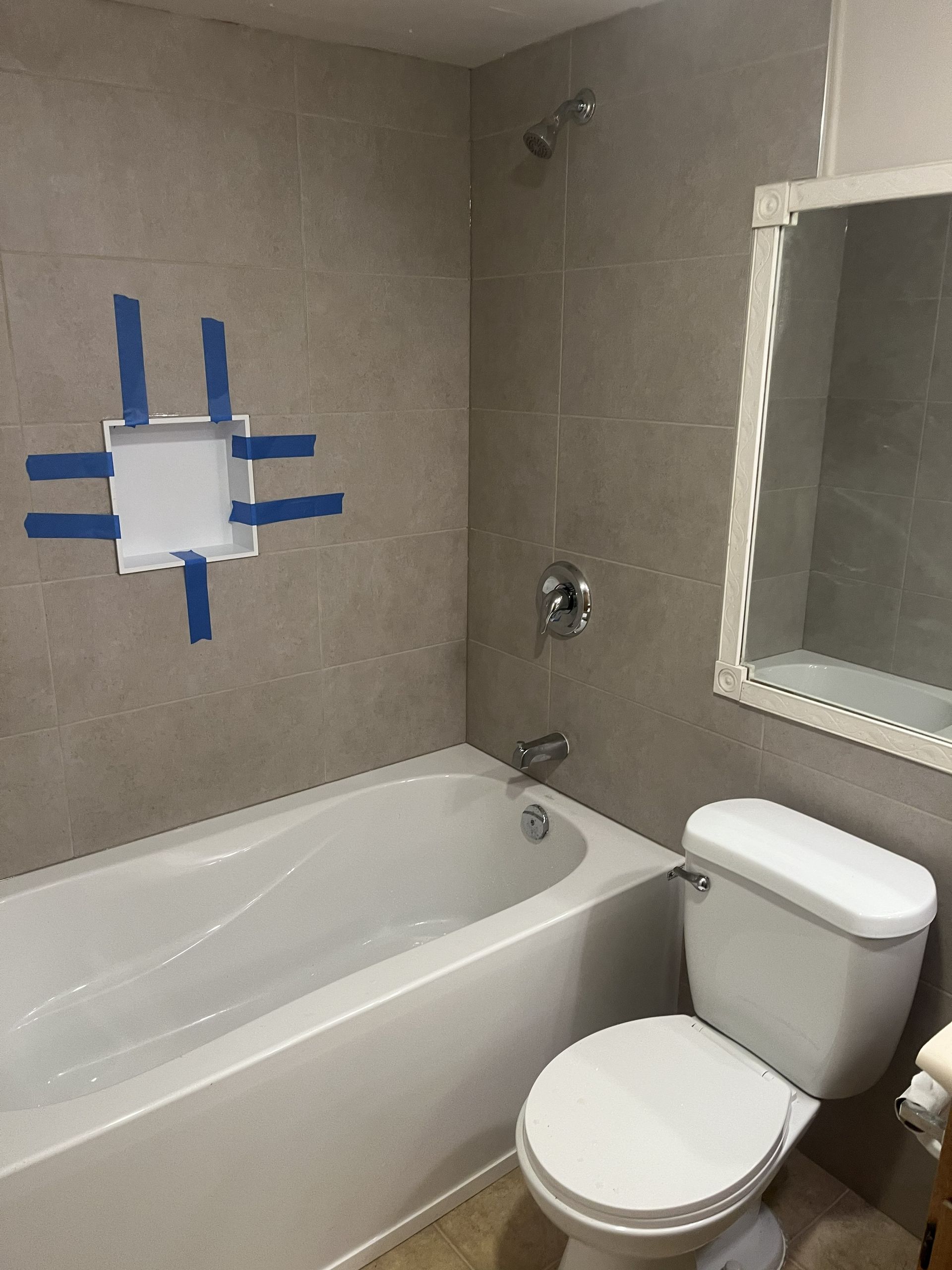 Bathroom with bathtub, toilet, and taped-over wall opening for repair.