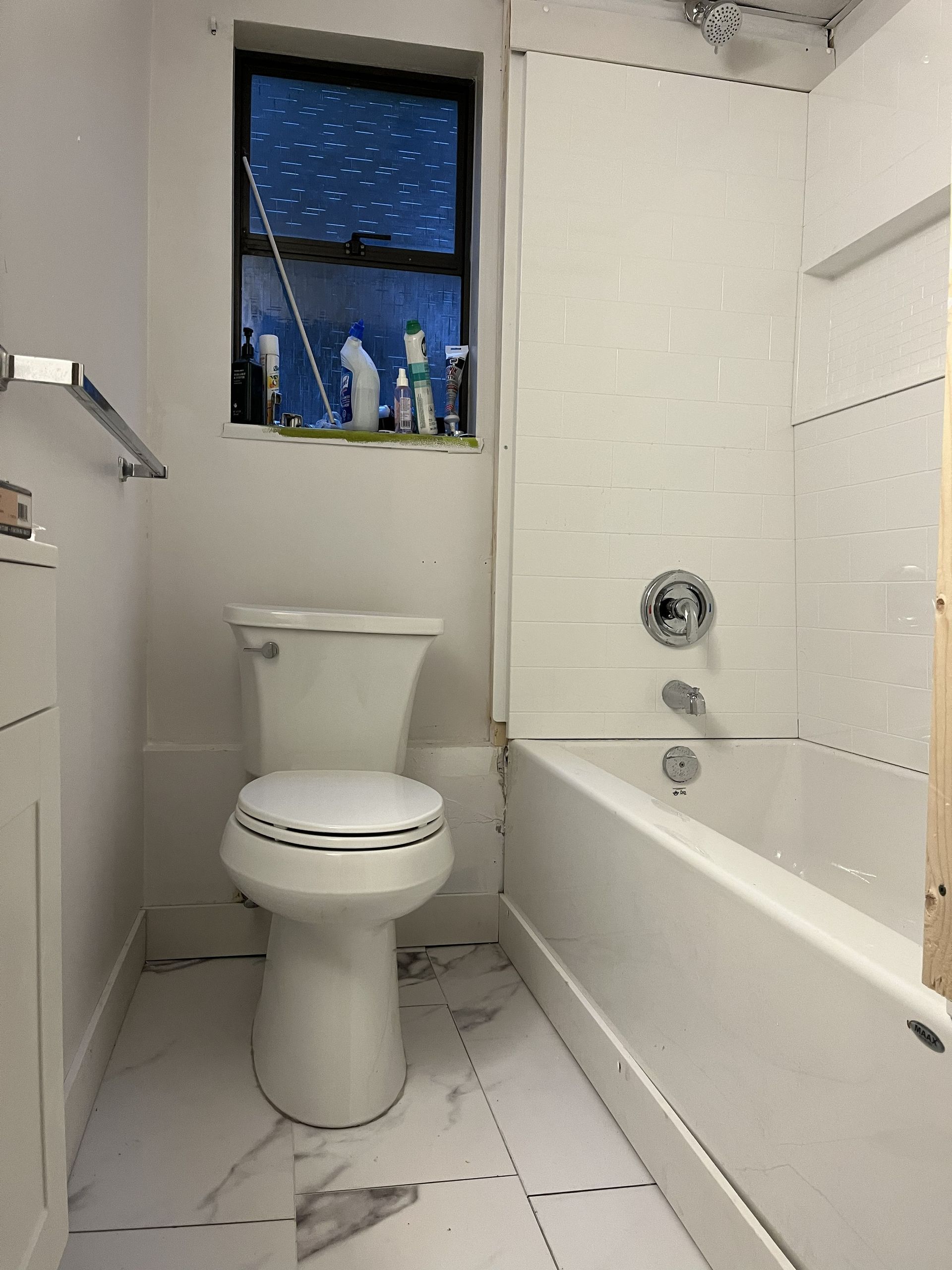 Small white bathroom with toilet, bathtub, and window showing a dark blue night sky.