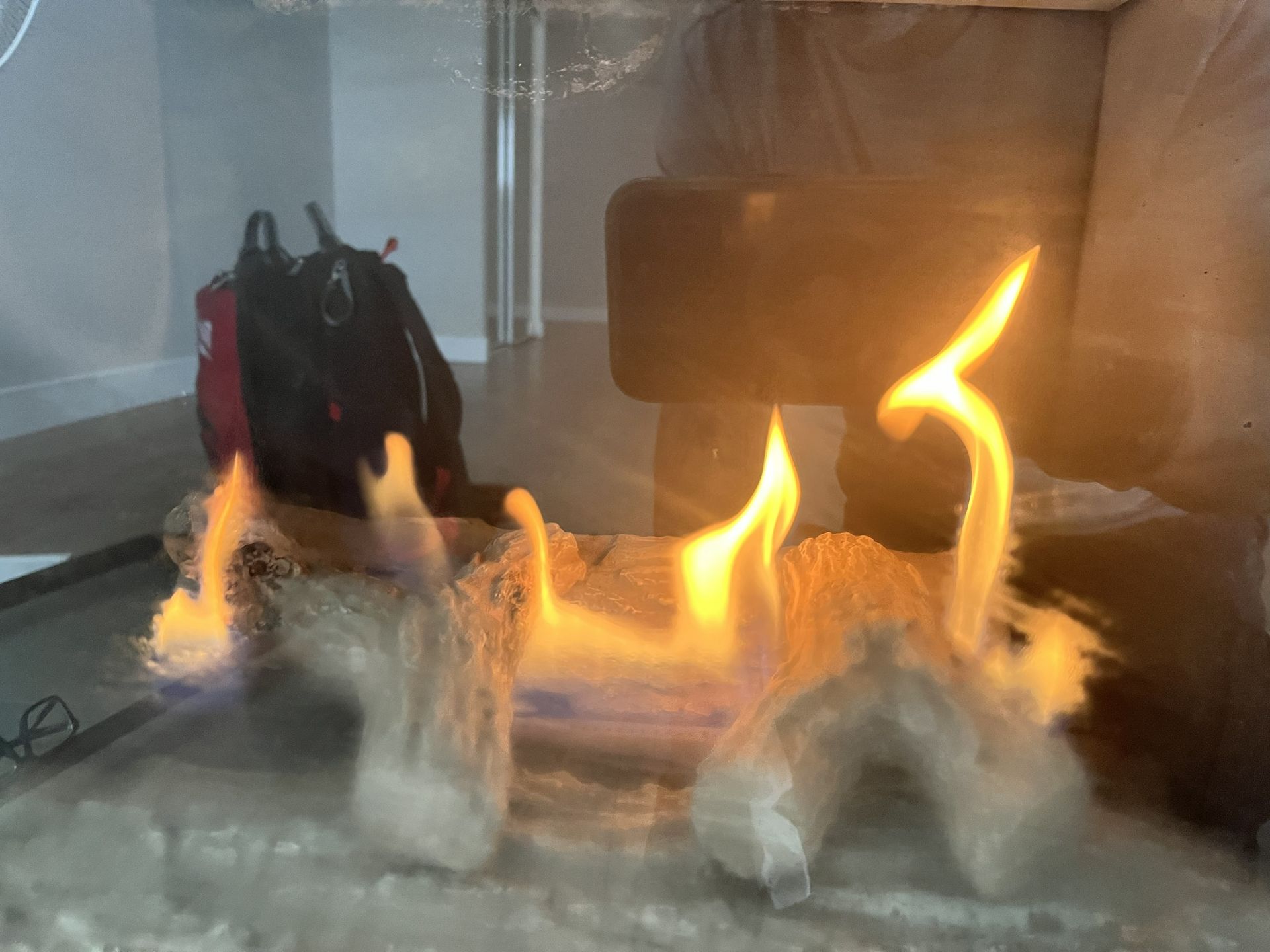 Small flames burning across a tabletop with a black backpack in the background indoors