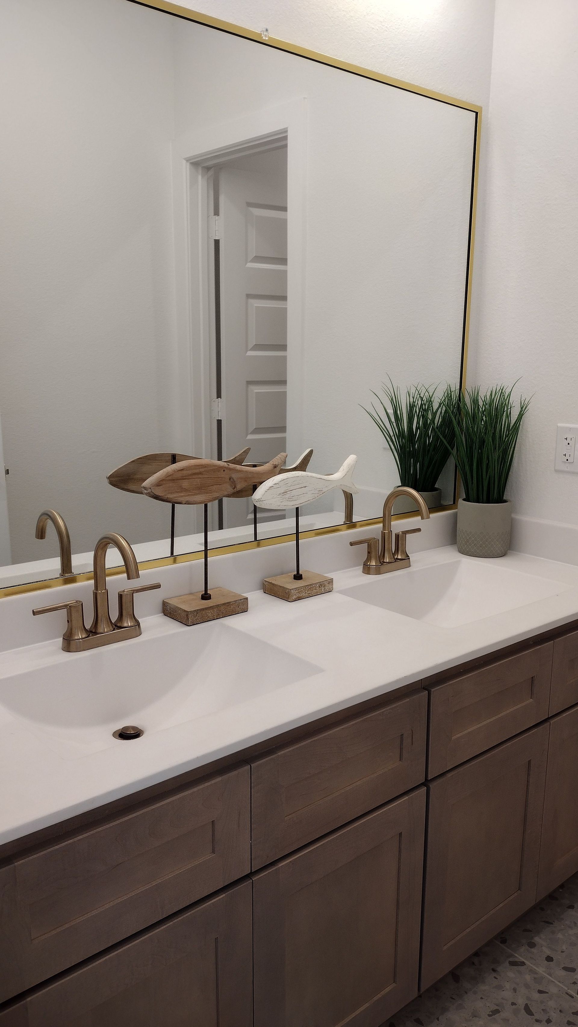 Modern bathroom vanity with large mirror, gold faucets, white countertop, and potted plant.