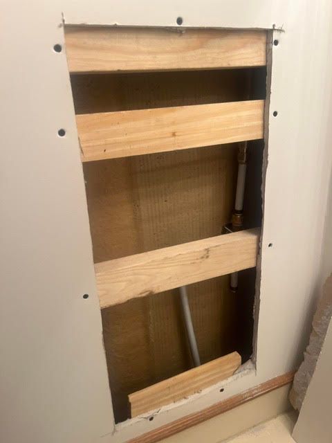 Open wall cavity with exposed wooden studs and wiring, framed by white drywall.