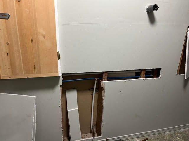 Partially demolished kitchen wall with exposed studs and a wooden cabinet on the left