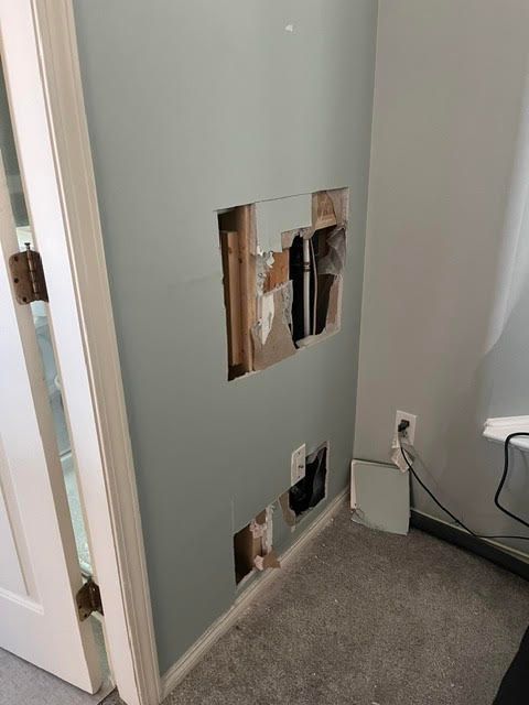 Damaged wall with holes exposing wiring beside a doorway and carpeted floor.