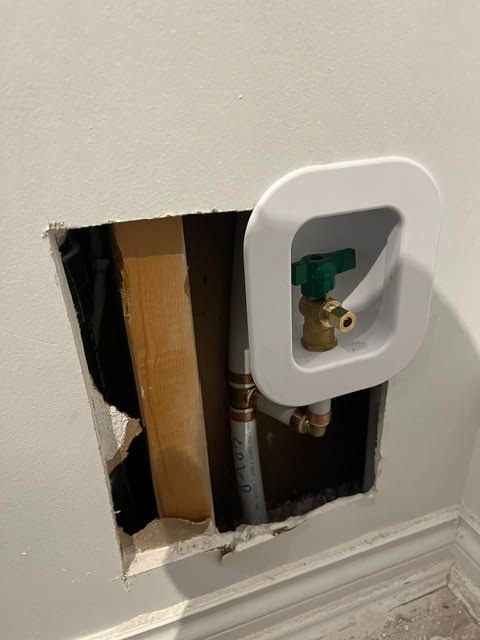 Wall cut open around plumbing with a green shutoff valve and exposed pipes.