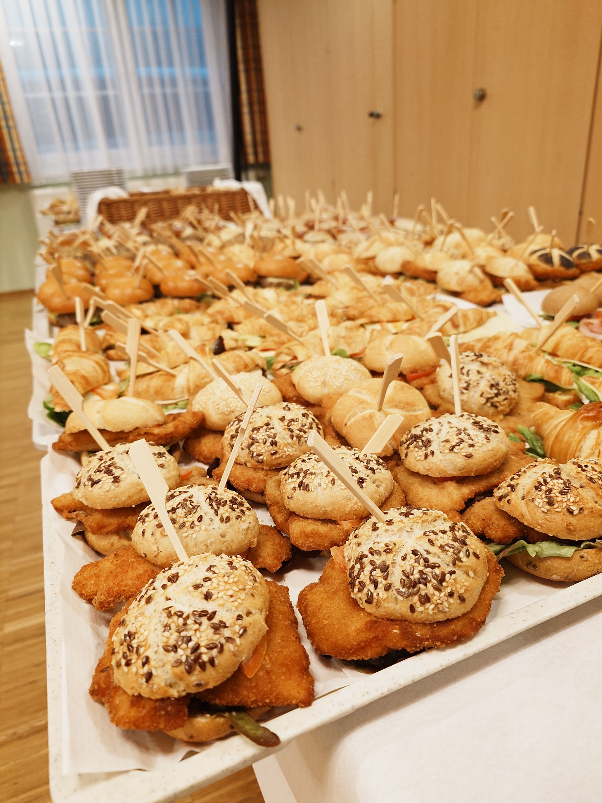 Platte mit verschiedenen Mini-Sandwiches und Gebäckstücken auf einem Tisch, garniert mit Samen und Zahnstochern