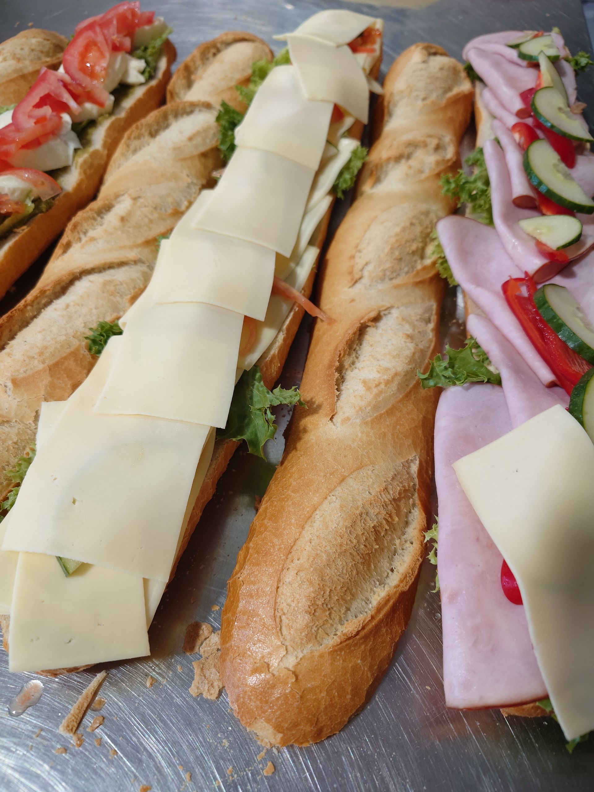 Drei Baguette-Sandwiches mit Käsescheiben, Salat, Tomaten und Gewürzgurken auf einem Tablett