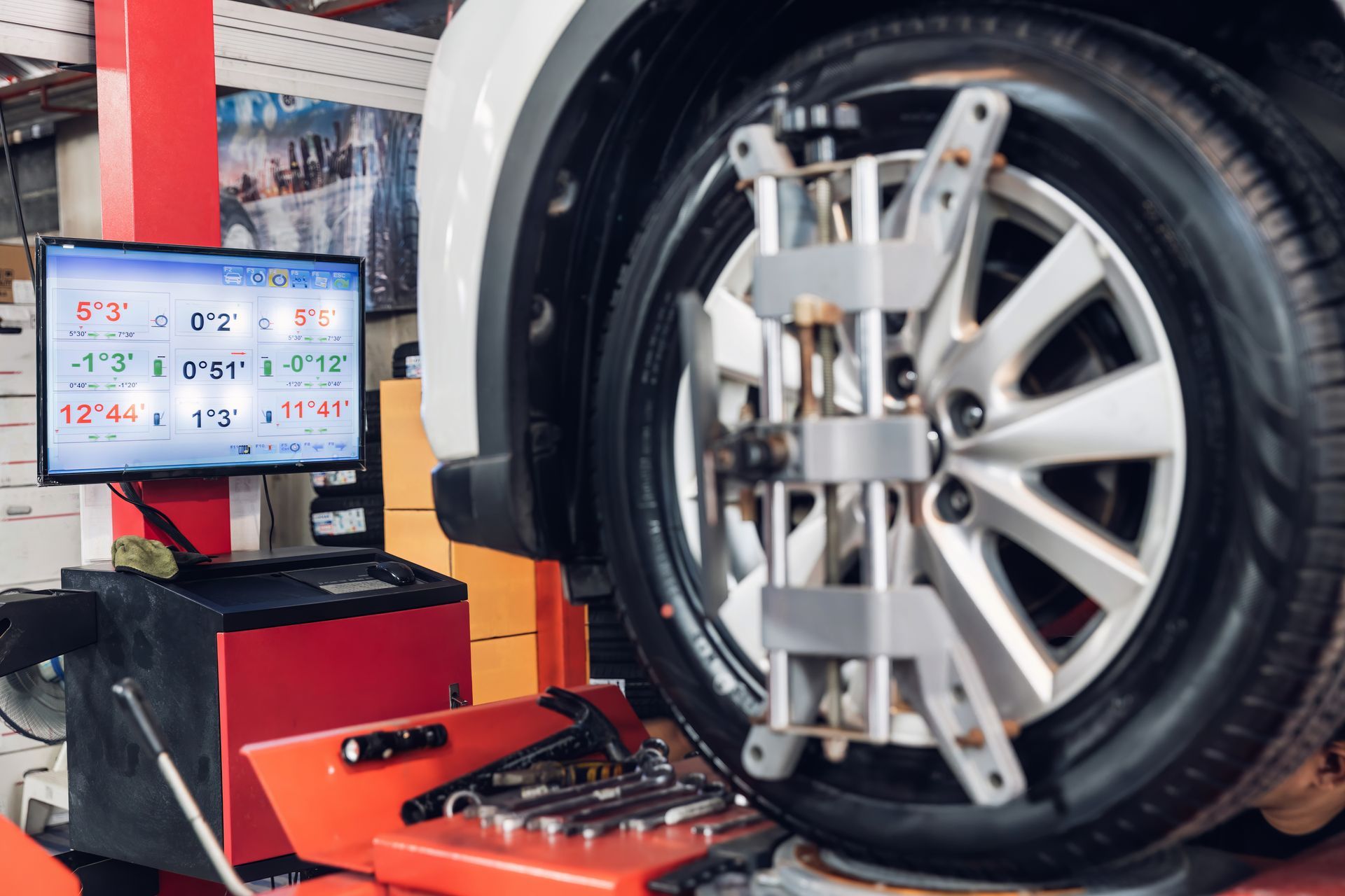 Car wheel alignment machine checking a tire in an auto repair shop, with a monitor displaying measurements.