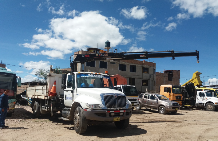 Camiones de construcción y trabajadores en una obra bajo un cielo azul brillante.
