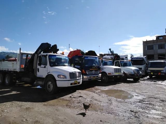 Grúas y camiones de trabajo estacionados en un terreno embarrado bajo un cielo azul brillante.