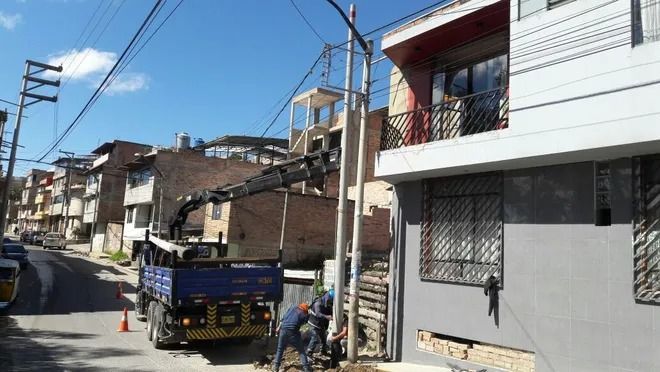 Calle estrecha con camión estacionado, casas y líneas eléctricas aéreas en un día soleado.
