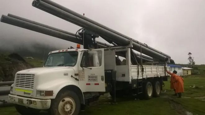 Camioneta blanca de servicio con grandes tubos negros en la parte superior, estacionada en un campo de hierba 