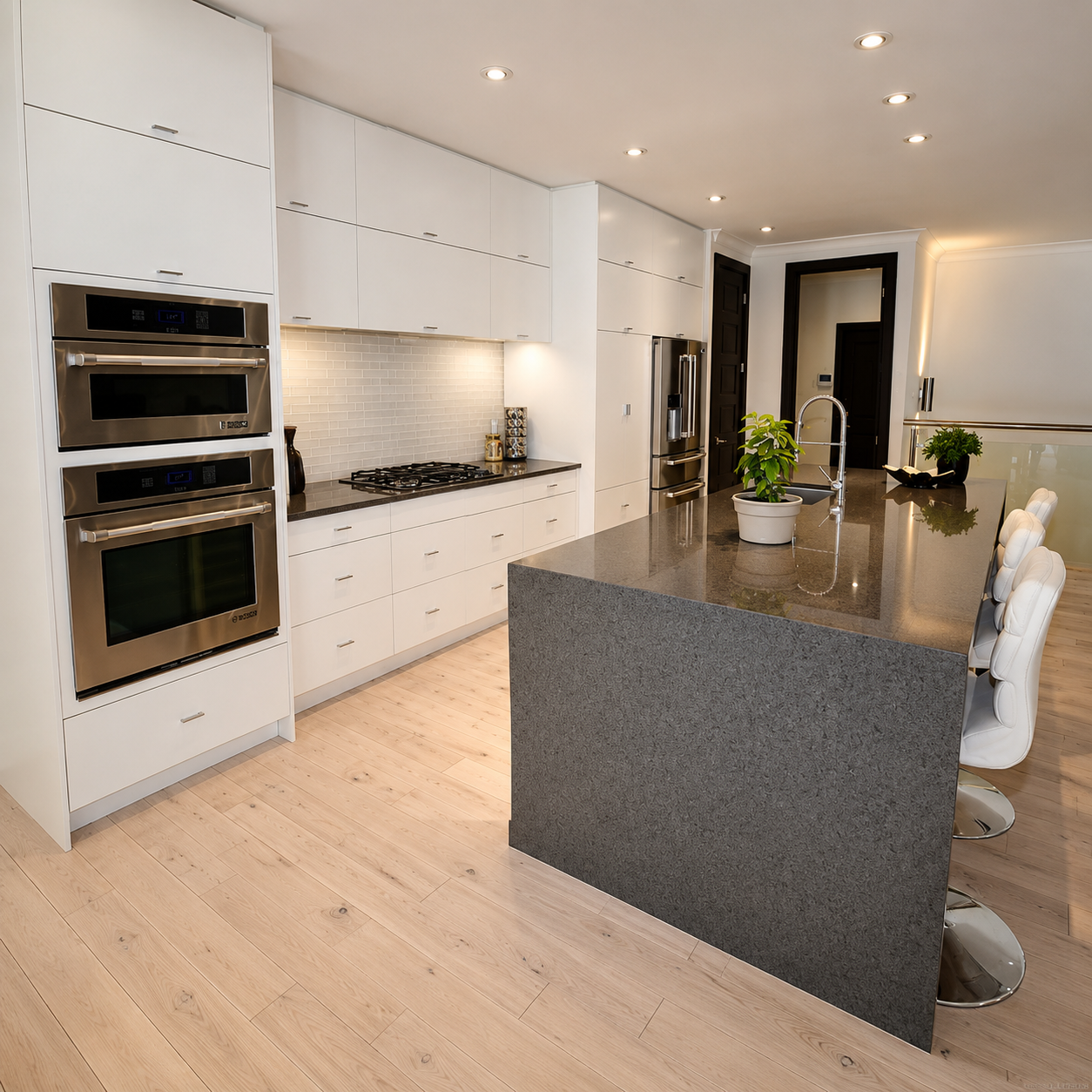 Modern white kitchen with a large gray island, built-in ovens, and light wood floors
