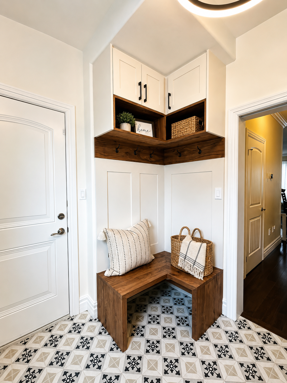 Small entryway with white doors, built-in wooden bench, patterned floor tile, and upper storage cabinets.