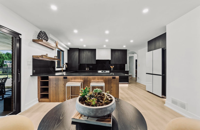 Bright modern kitchen with black cabinets, wood island, and a potted plant on a round table in the foreground
