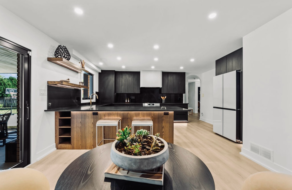 Modern open kitchen with black cabinets, white walls, wood floors, and a small table in the foreground
