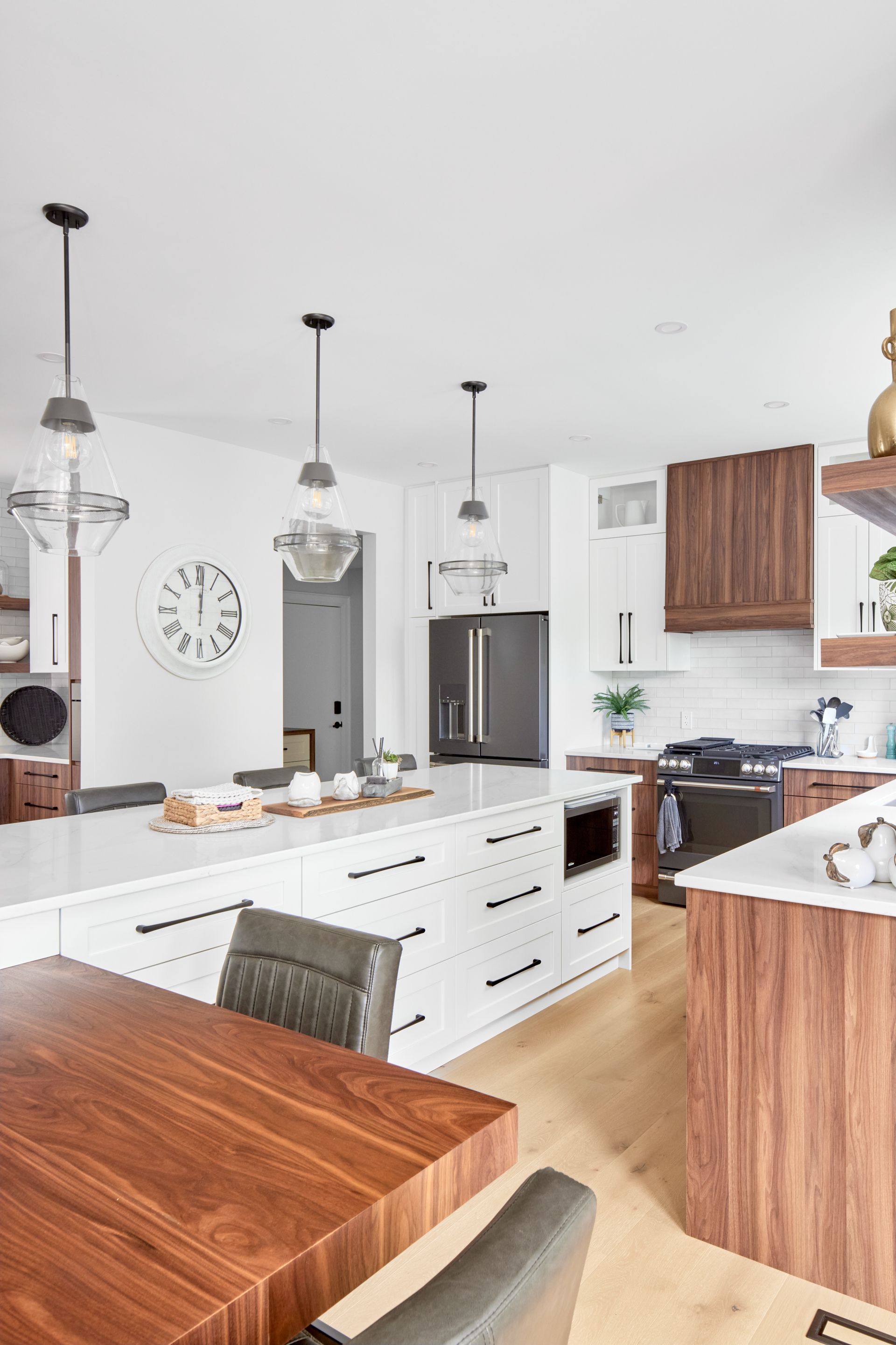 Modern kitchen with white island, wood accents, pendant lights, and stainless steel refrigerator.