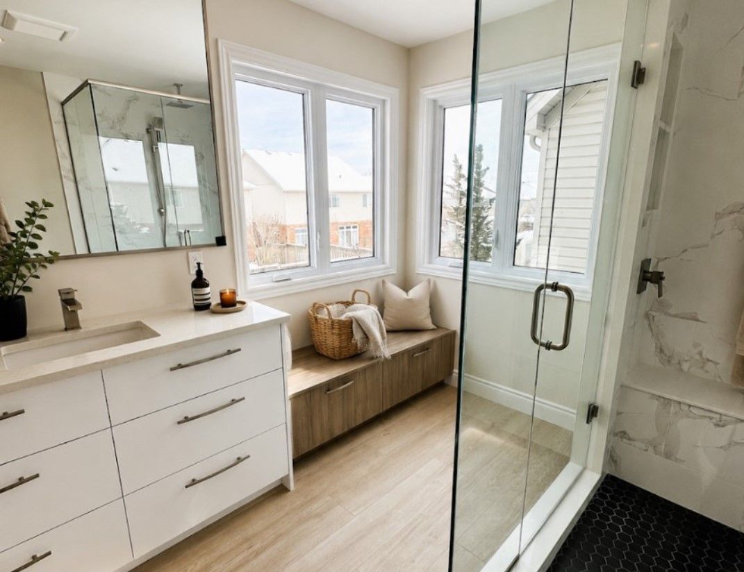 Bright modern bathroom with double vanity, glass shower, and bench by windows