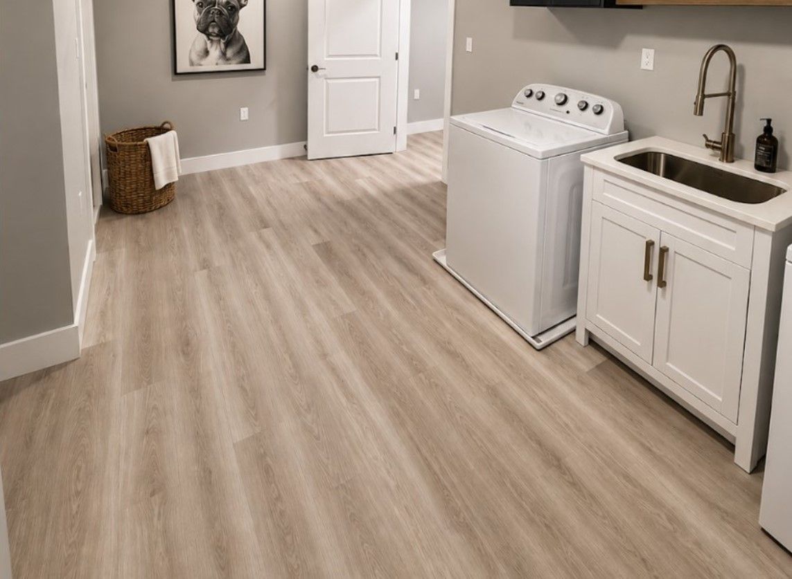 Laundry room with light wood flooring, washer, sink cabinet, and a laundry basket near the door.