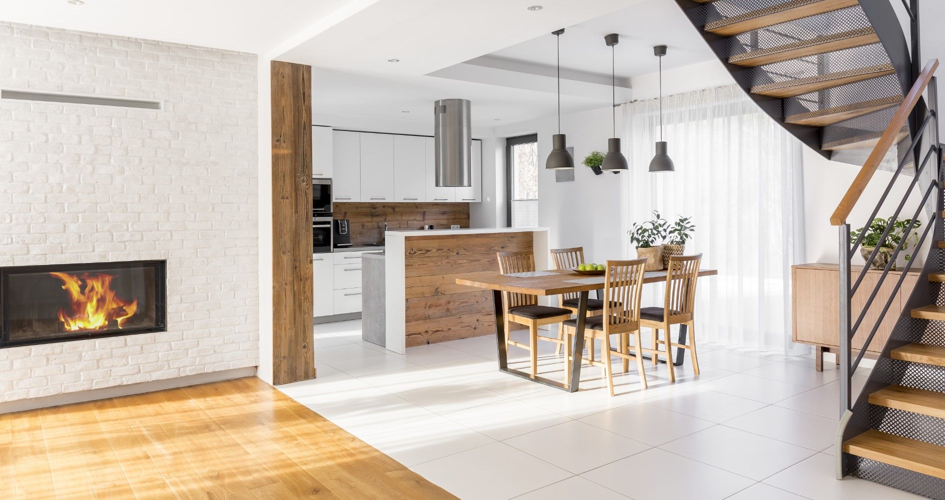 Modern open-plan living room with fireplace, kitchen island, dining table, and staircase with plants