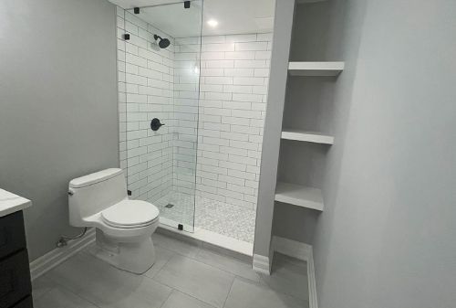 Modern bathroom with toilet, glass shower, white tile walls, and built-in shelving.