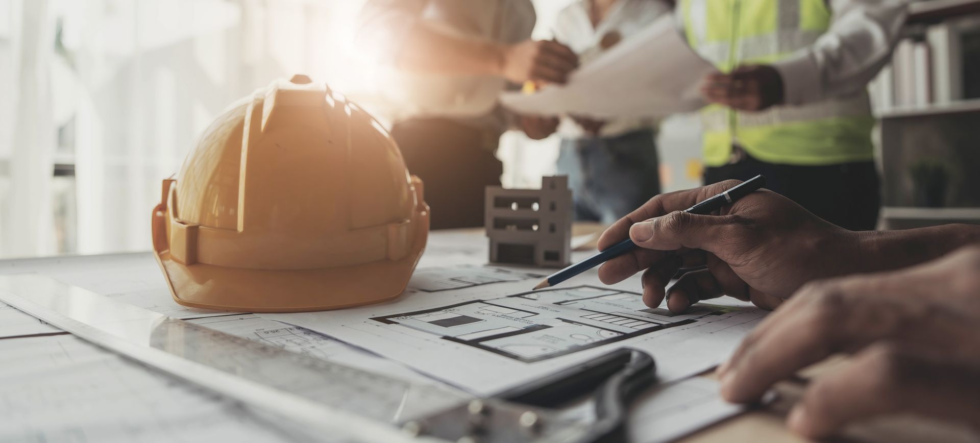 Construction hard hat and hands using a calculator over blueprints on a desk