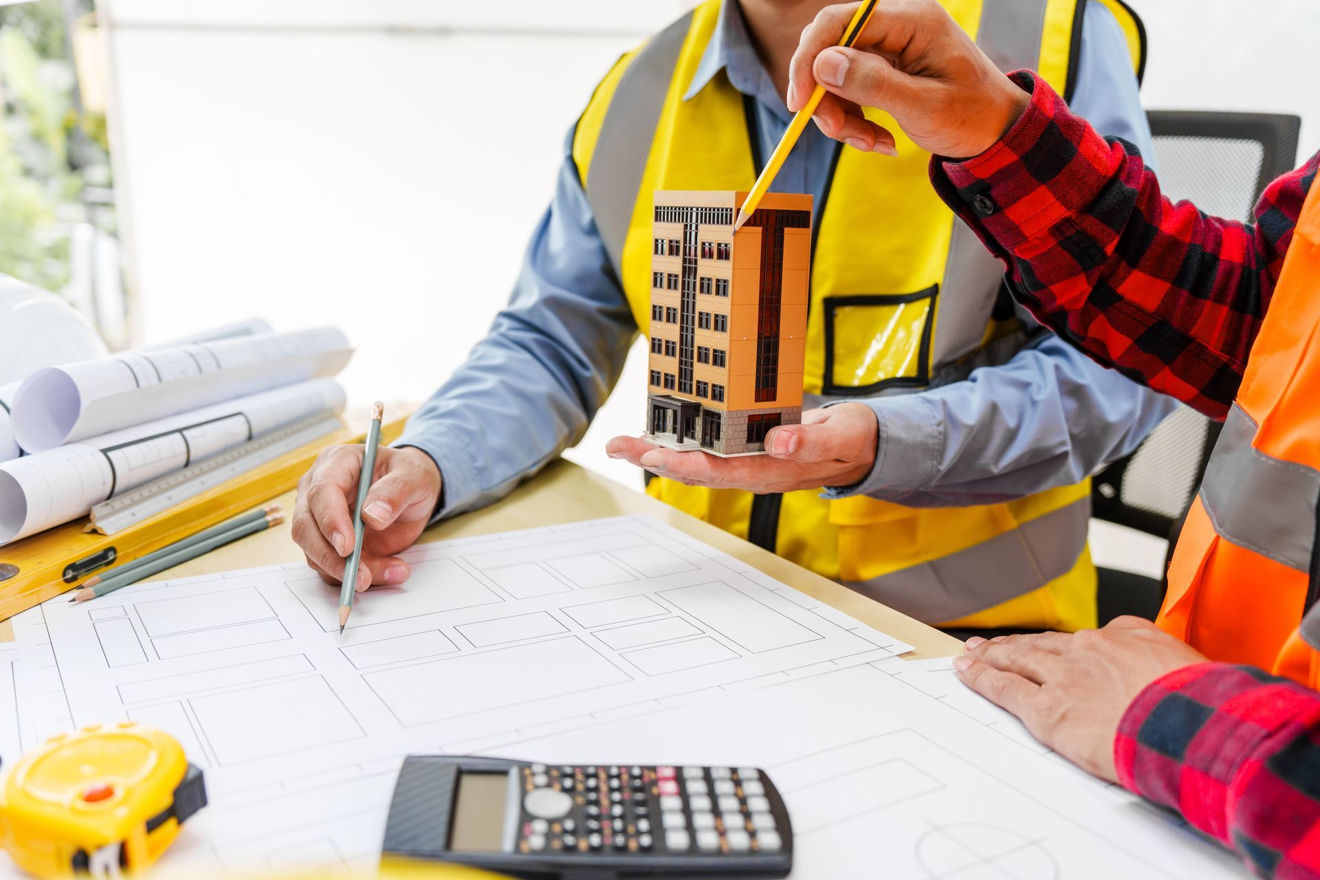Engineers reviewing building plans with a calculator and architectural model at a worktable