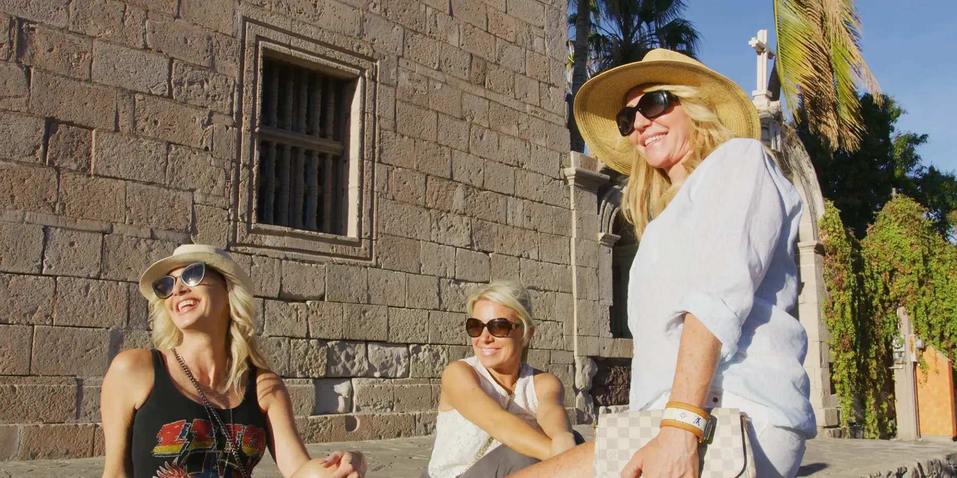 Community in Loreto three women from danzante bya wearing hats and sunglasses are standing in front of a stone building in loreto, mexico