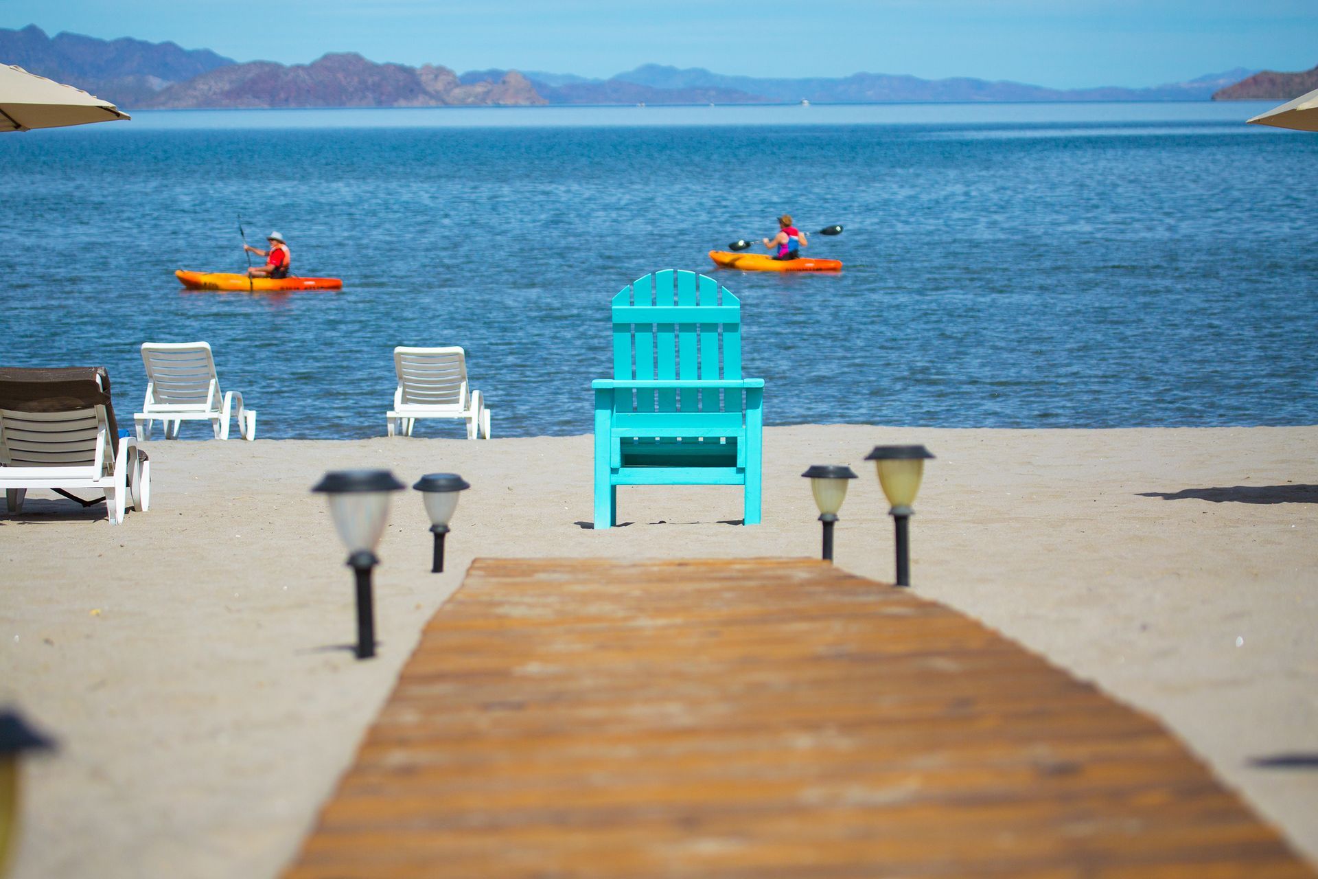 A blue chair is sitting on the beach next to a wooden dock.
