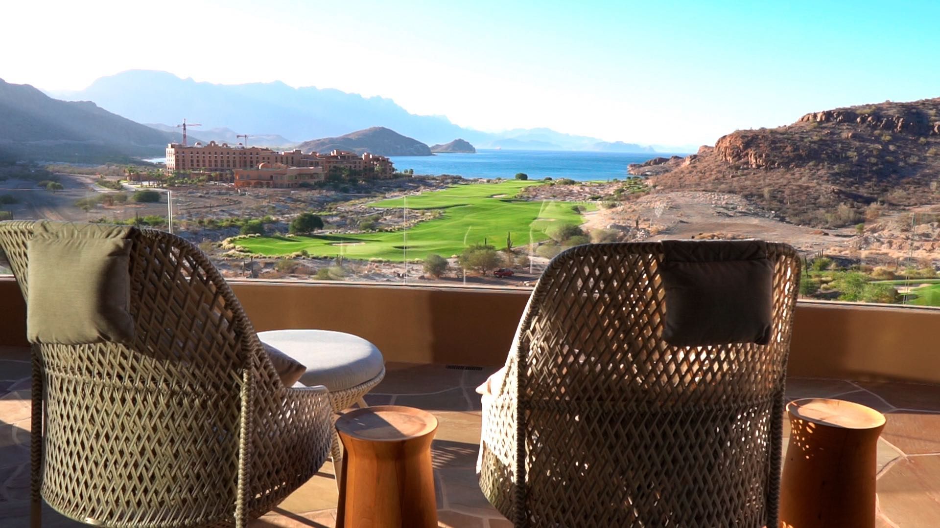Two chairs are sitting on a balcony overlooking the ocean and mountains.