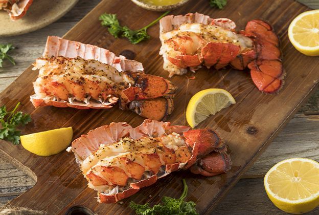Three lobsters are sitting on a wooden cutting board with lemon slices.