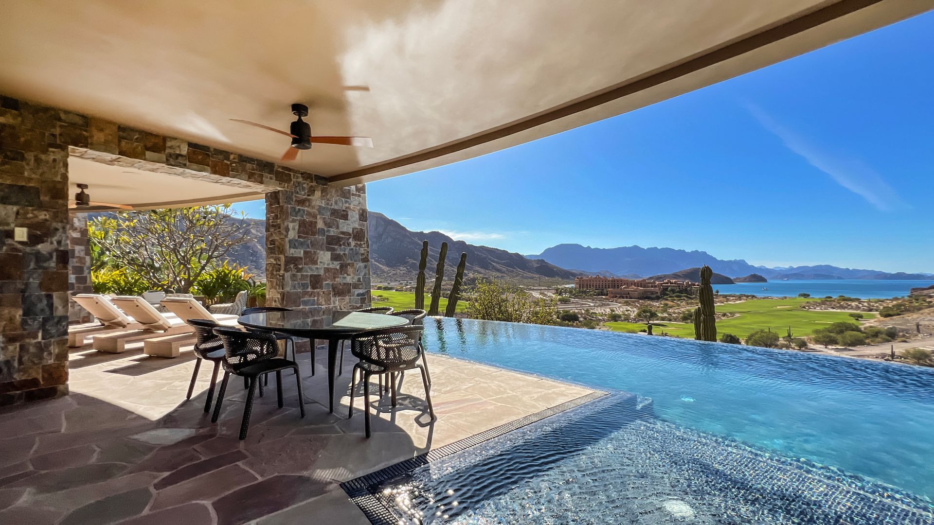 There is a swimming pool with a view of the ocean and mountains.