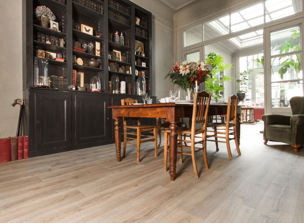 Eetkamer met houten tafel, stoelen en een ingebouwde zwarte boekenkast, vlak bij een lichte serre.