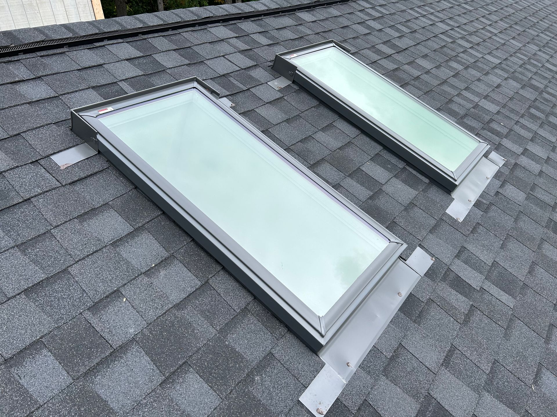 Two rectangular skylights installed on a gray shingled roof with metal flashing.