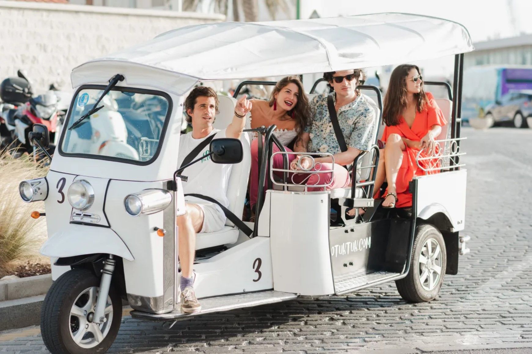 Four people riding in a white tuk-tuk in Brisbane on a cobblestone street; smiling and enjoying themselves.