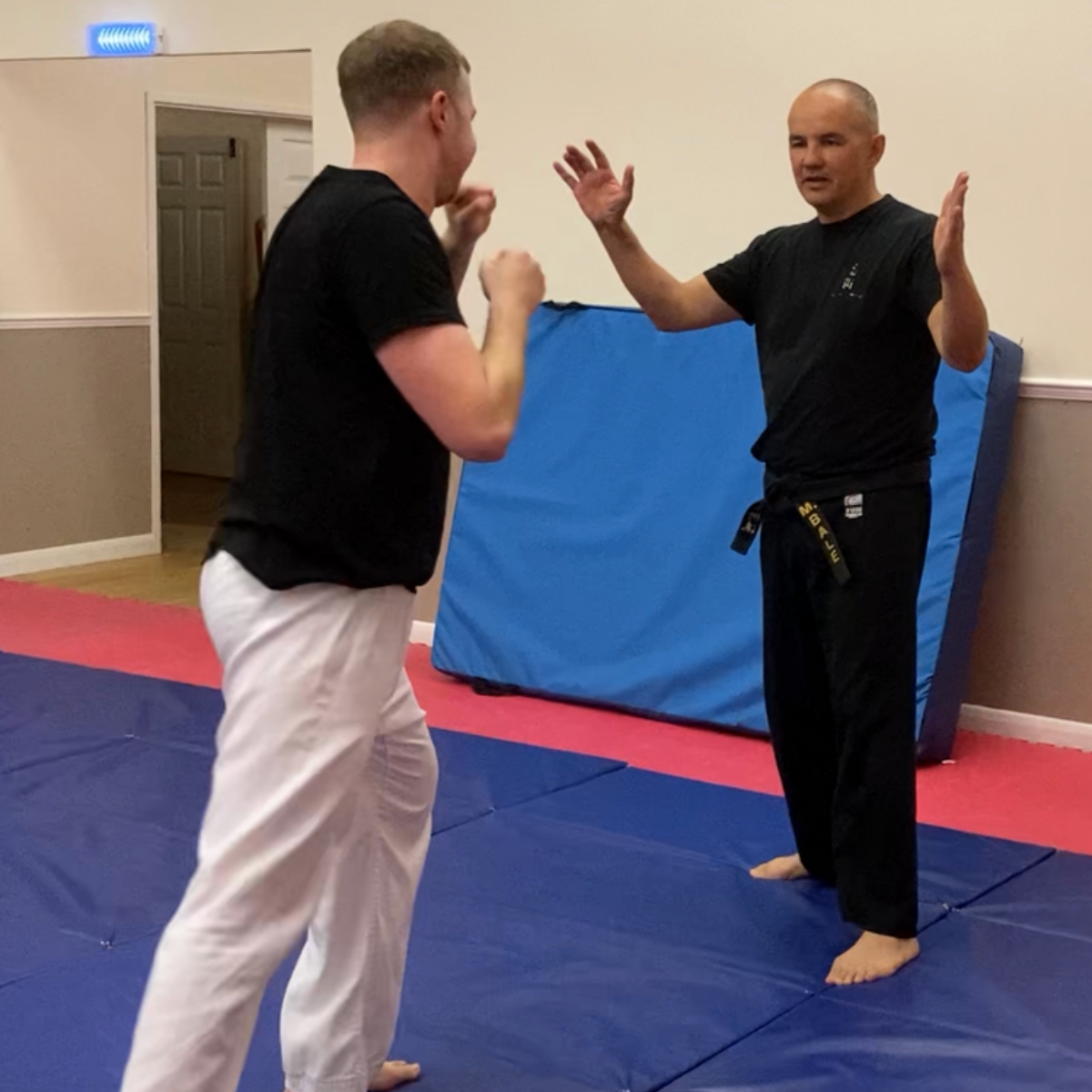 Two men are standing on a mat in a room with a blue mat in the background