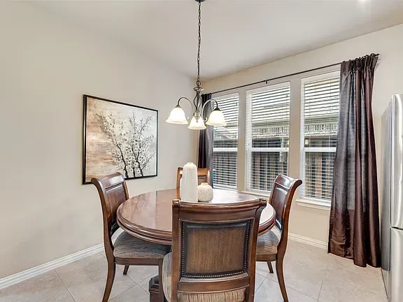 Dining room with round wooden table, four chairs, pendant lights, framed art, and a window with curtains.